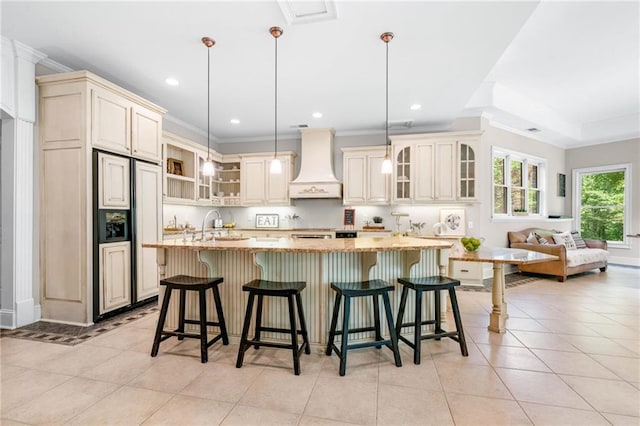 kitchen with premium range hood, paneled refrigerator, cream cabinets, a large island with sink, and light tile patterned floors
