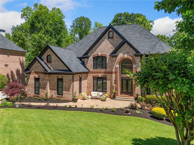 french provincial home featuring brick siding, a front yard, a patio area, and outdoor lounge area