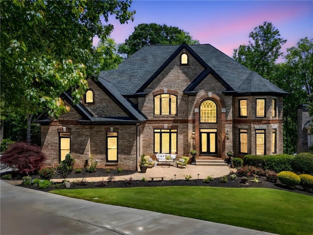 french country style house featuring a lawn, brick siding, and french doors