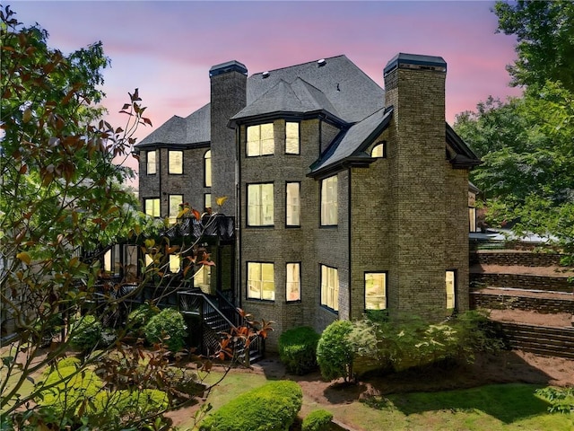 back of property at dusk with a chimney and stairs