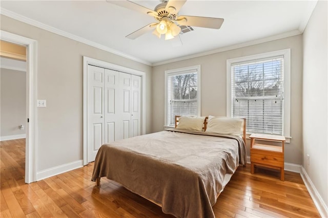 bedroom with a closet, ornamental molding, a ceiling fan, light wood-type flooring, and baseboards