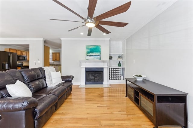 living area featuring light wood-style flooring, ceiling fan, a fireplace with flush hearth, vaulted ceiling, and crown molding