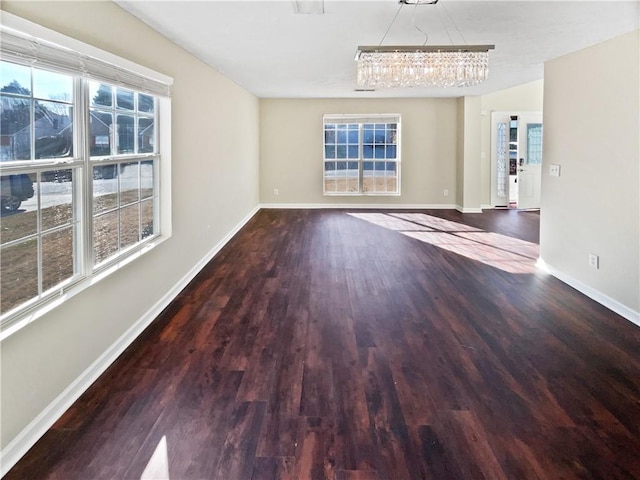 unfurnished living room with a wealth of natural light, a chandelier, and dark hardwood / wood-style floors