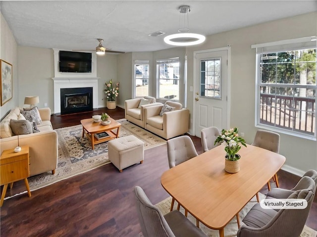 dining space featuring ceiling fan, a large fireplace, and dark wood-type flooring