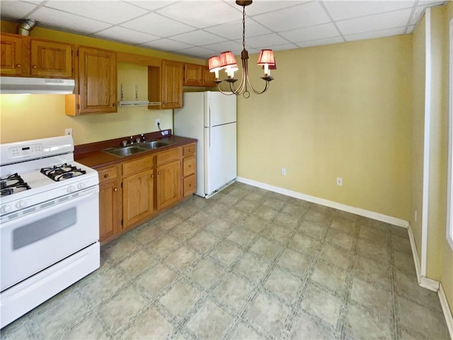 kitchen featuring a drop ceiling, white appliances, sink, pendant lighting, and an inviting chandelier