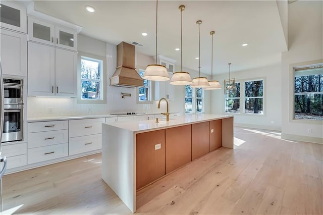 kitchen featuring white cabinetry, sink, an island with sink, and custom range hood