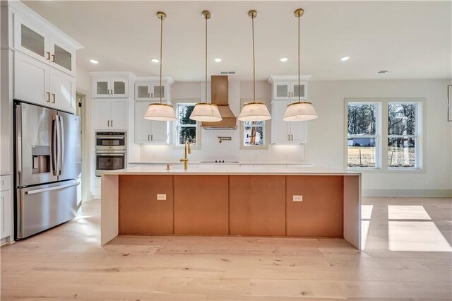 kitchen featuring premium range hood, pendant lighting, white cabinetry, a kitchen island with sink, and stainless steel appliances