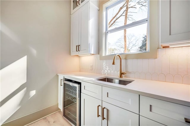 kitchen with sink, backsplash, wine cooler, light hardwood / wood-style floors, and white cabinets