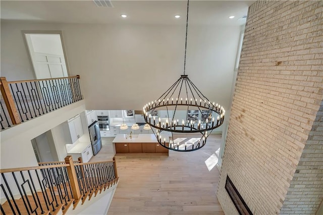 interior space featuring hardwood / wood-style flooring, a towering ceiling, brick wall, and an inviting chandelier