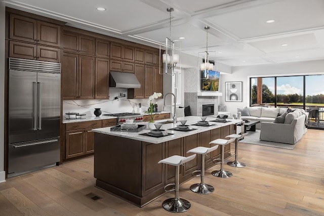 kitchen featuring a kitchen breakfast bar, coffered ceiling, stainless steel built in fridge, a center island with sink, and light wood-type flooring