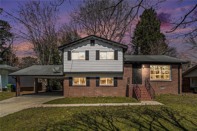 tri-level home featuring an attached carport, brick siding, driveway, and a front lawn