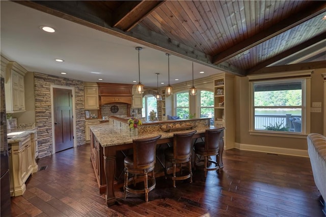 kitchen featuring dark wood-style flooring, cream cabinets, light stone countertops, a large island with sink, and baseboards