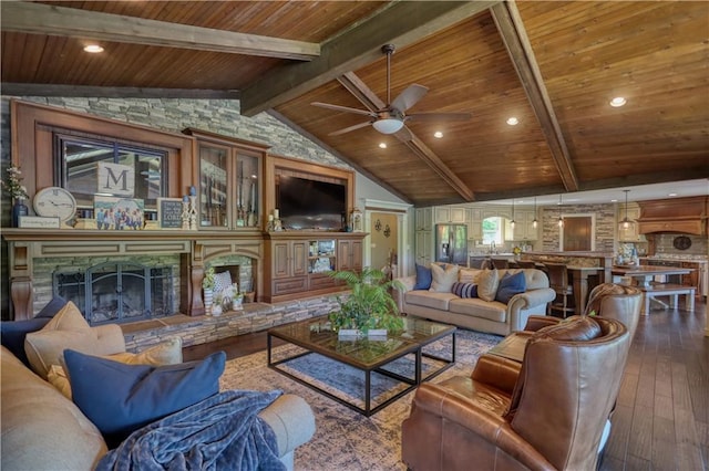 living room featuring ceiling fan, lofted ceiling with beams, wood-type flooring, a stone fireplace, and wooden ceiling