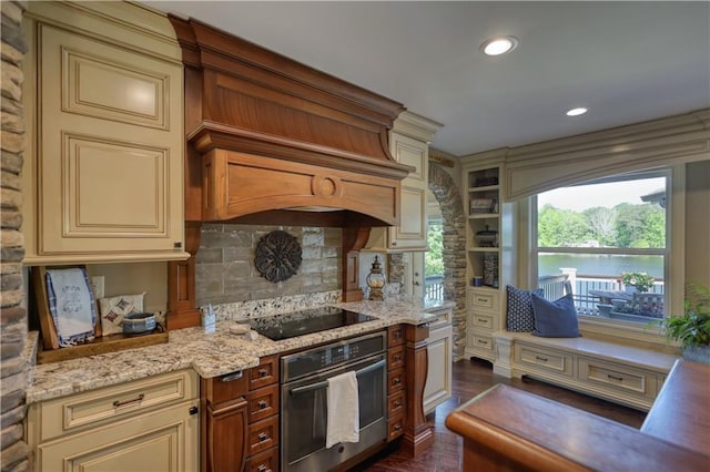 kitchen featuring wall oven, black electric cooktop, cream cabinets, light stone counters, and backsplash
