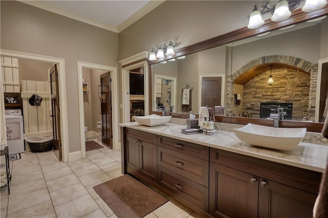 bathroom with crown molding, double vanity, washer / dryer, a stone fireplace, and a sink