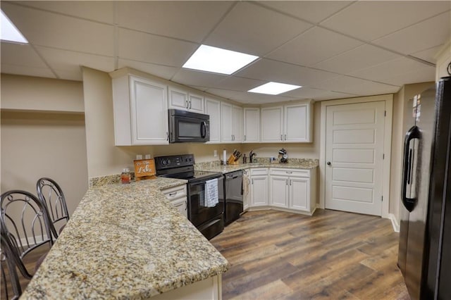 kitchen with white cabinets, a peninsula, a drop ceiling, dark wood-type flooring, and black appliances