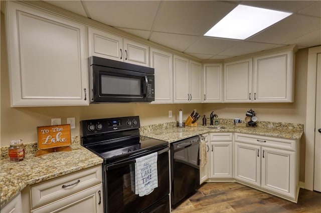 kitchen featuring light stone counters, a sink, a drop ceiling, wood finished floors, and black appliances