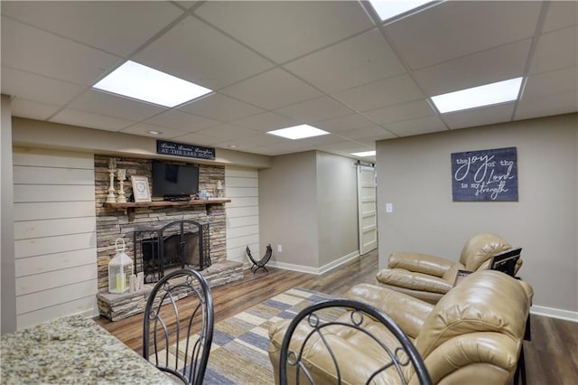 living room featuring baseboards, a stone fireplace, wood finished floors, and a paneled ceiling