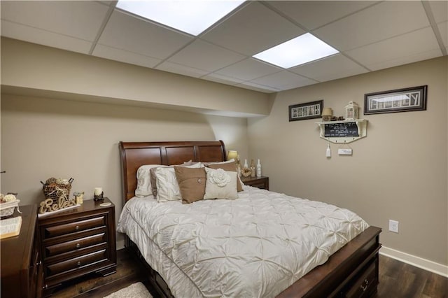 bedroom featuring baseboards, a drop ceiling, and dark wood-style floors