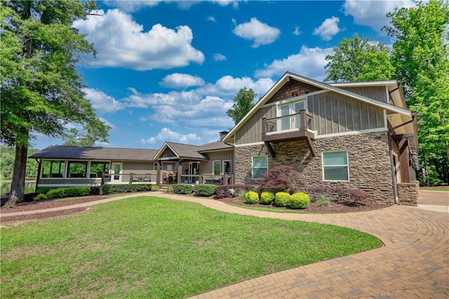 craftsman inspired home featuring a balcony, board and batten siding, a front yard, and stone siding