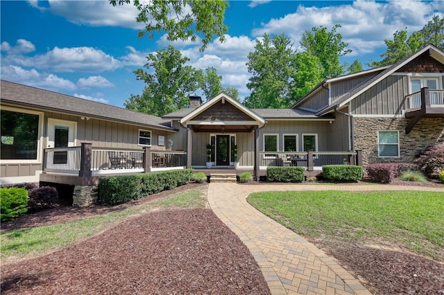 rear view of house featuring board and batten siding, a chimney, a lawn, a wooden deck, and stone siding