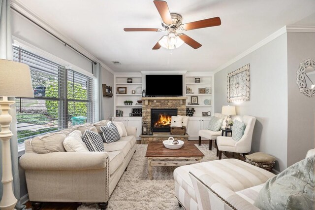 living room featuring crown molding, a fireplace, built in features, a ceiling fan, and visible vents