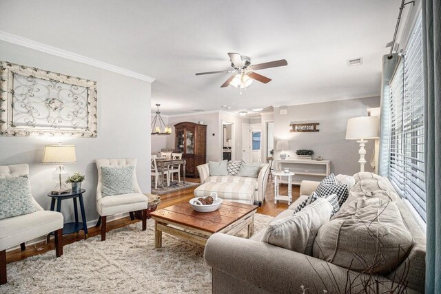 living area featuring visible vents, ornamental molding, wood finished floors, baseboards, and ceiling fan with notable chandelier
