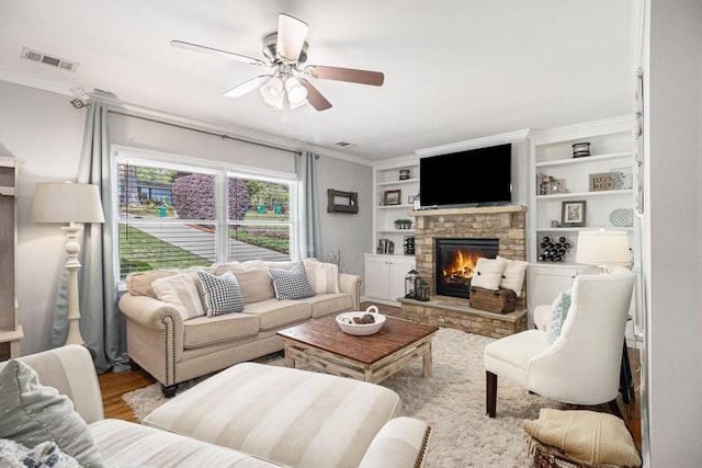 living room featuring ceiling fan, visible vents, crown molding, a fireplace, and wood finished floors