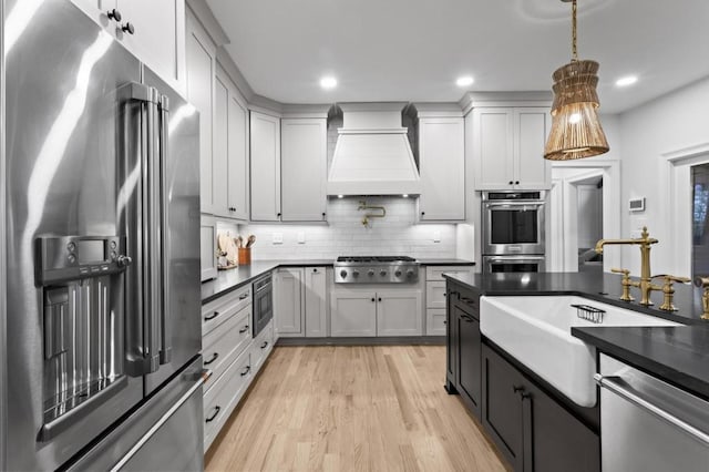 kitchen with pendant lighting, sink, backsplash, stainless steel appliances, and custom exhaust hood