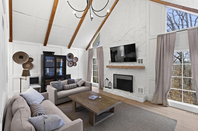 living room featuring an inviting chandelier, beam ceiling, high vaulted ceiling, wood-type flooring, and a stone fireplace