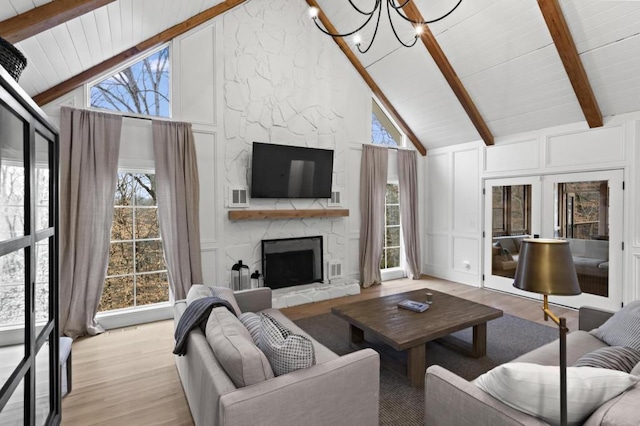 living room featuring high vaulted ceiling, a fireplace, light hardwood / wood-style floors, beamed ceiling, and a chandelier