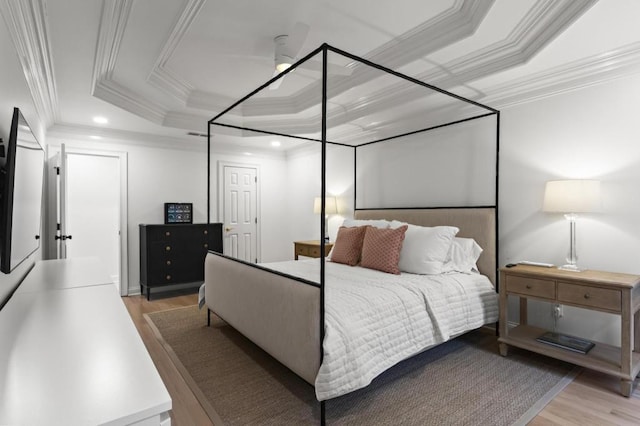 bedroom with ornamental molding, a tray ceiling, and light hardwood / wood-style flooring