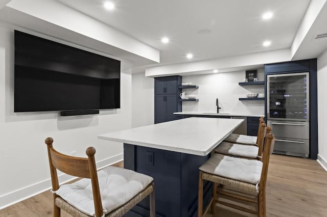 bar featuring blue cabinets, beverage cooler, light hardwood / wood-style floors, and sink