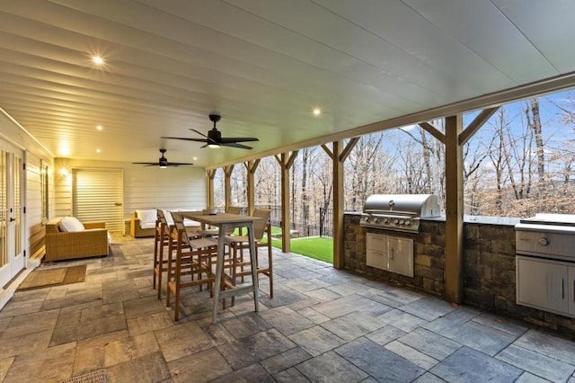 patio terrace at dusk with an outdoor kitchen, a grill, and ceiling fan