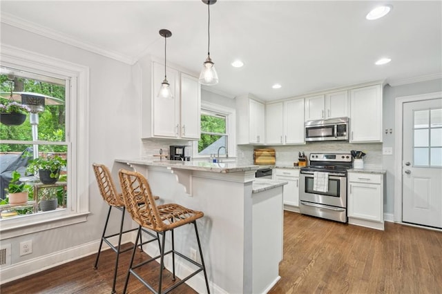 kitchen featuring a peninsula, a breakfast bar area, white cabinets, appliances with stainless steel finishes, and backsplash