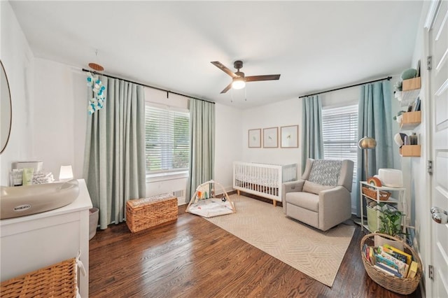 bedroom featuring a ceiling fan, a crib, wood finished floors, and radiator