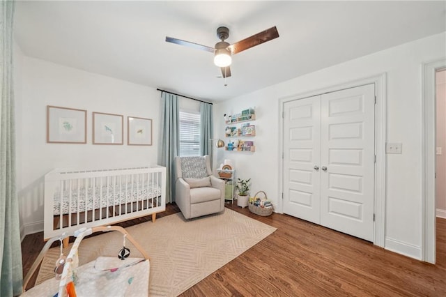 bedroom with a nursery area, radiator, a ceiling fan, wood finished floors, and a closet
