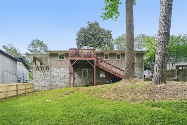 rear view of house with fence, stone siding, a wooden deck, stairway, and a lawn