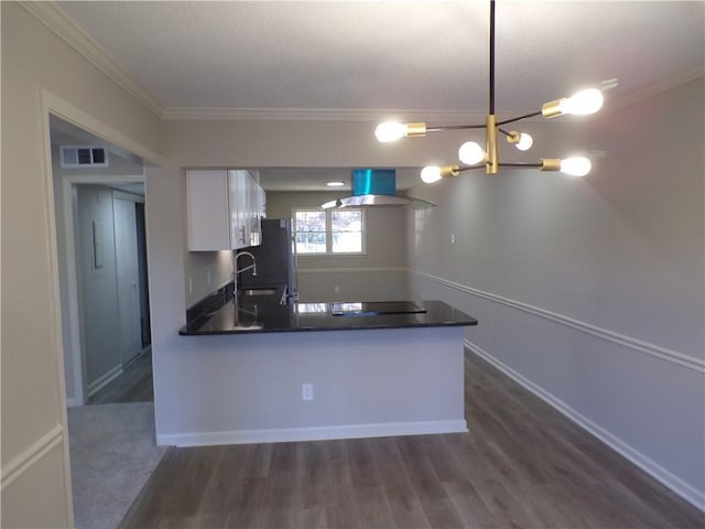 kitchen with dark countertops, wall chimney range hood, white cabinetry, and visible vents