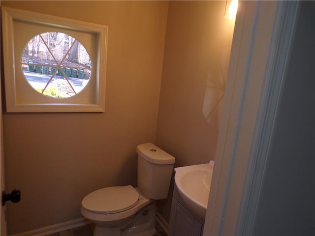 half bathroom with toilet, baseboards, and vanity