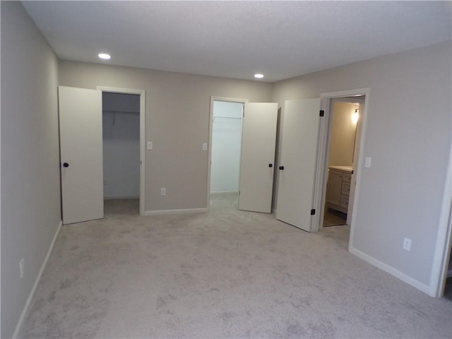 unfurnished bedroom featuring baseboards, light colored carpet, ensuite bath, a walk in closet, and recessed lighting