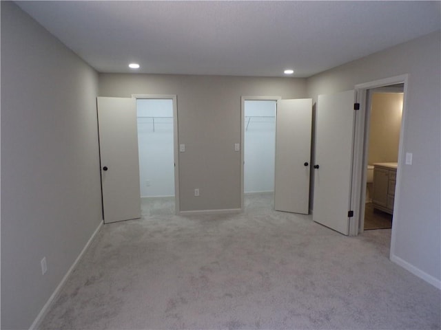 unfurnished bedroom featuring light carpet, a spacious closet, baseboards, and recessed lighting