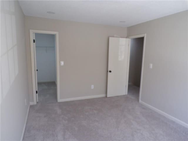 unfurnished bedroom featuring carpet floors, a spacious closet, baseboards, and a closet