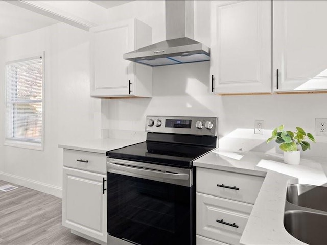 kitchen featuring white cabinetry, stainless steel range with electric stovetop, wall chimney exhaust hood, light hardwood / wood-style floors, and light stone counters