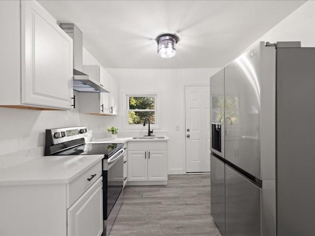 kitchen with light hardwood / wood-style flooring, wall chimney exhaust hood, white cabinets, and appliances with stainless steel finishes