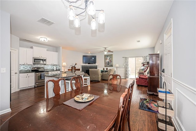 dining area with dark wood finished floors, ceiling fan with notable chandelier, and visible vents