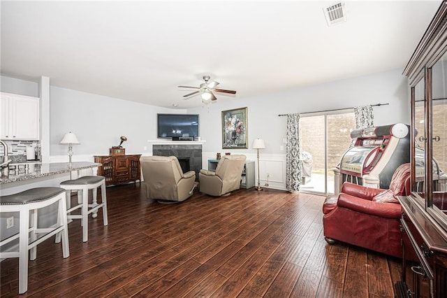 living room featuring a tiled fireplace, dark wood-type flooring, a ceiling fan, and visible vents