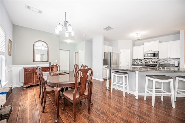 dining room featuring a chandelier, visible vents, dark wood finished floors, and a wainscoted wall