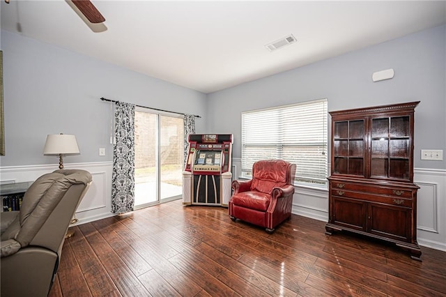 sitting room with visible vents, wainscoting, dark wood-type flooring, and ceiling fan