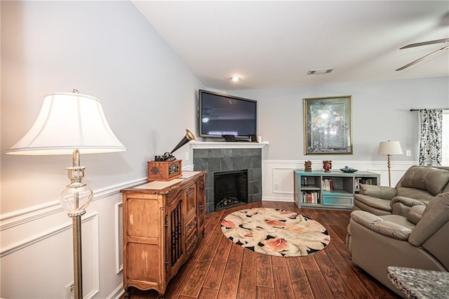 living room featuring visible vents, a wainscoted wall, a fireplace, a ceiling fan, and dark wood-style flooring